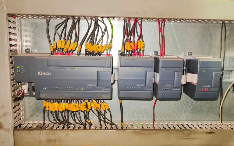 A row of compact controllers and expansion modules wired on a cabinet backplate with numbered ferrules